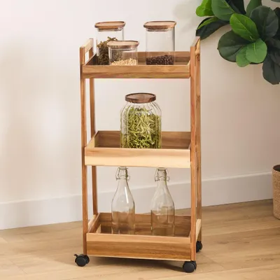 A wooden trolley with three shelves, containing jars and bottles.