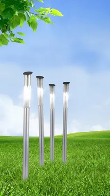 Four solar garden lights are placed in a grassy field under a blue sky with green leaves in the foreground.