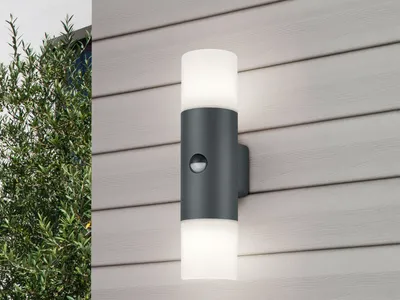 An outdoor LED wall light mounted on a wood-paneled wall, with greenery to the left.