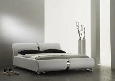 A modern white bed with black pillows in a minimalist room.