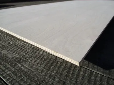 A close-up, angled view of a light-colored plywood sheet resting on a dark, textured surface.