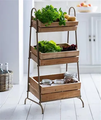 A three-tiered wooden crate shelving unit filled with fresh produce and jars, set against a bright, clean kitchen background.
