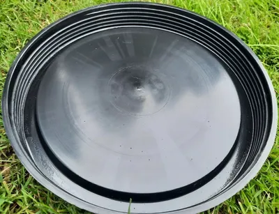 A black plastic lid is placed on green grass.
