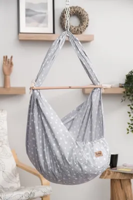 A baby hammock with a star pattern hangs from the ceiling, set against a neutral background with shelves and decor.
