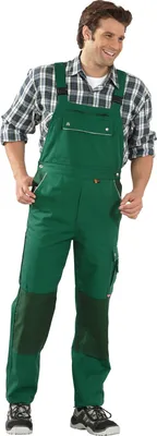 A man wearing green overalls and a plaid shirt, standing against a white background.