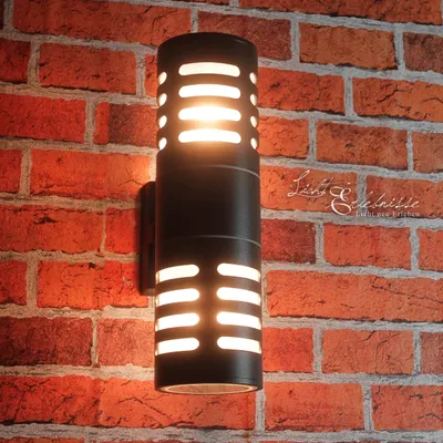 A black outdoor wall lamp with illuminated slots is mounted on a red brick wall.
