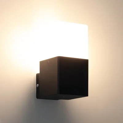 A modern black cube-shaped outdoor wall light with a white frosted glass top, mounted on a light gray wall.