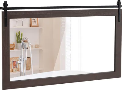 A rectangular mirror with a dark brown wooden frame and a black metal sliding barn door hardware is shown against a white background. The mirror reflects a bathroom scene with shelves, a plant, and a showerhead.