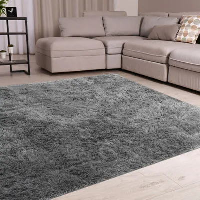 A fluffy gray rug in a living room setting with a sectional sofa in the background.