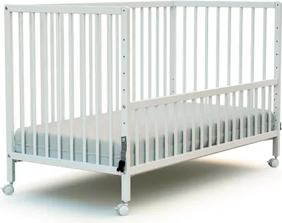 A white wooden baby crib with a mattress and wheels.