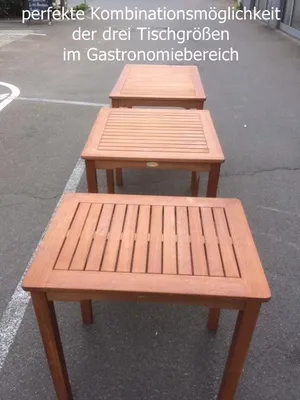 Three wooden tables of different sizes are arranged in a row on an asphalt surface.