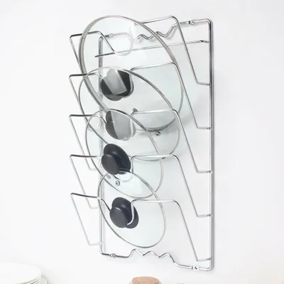 A wall-mounted rack holding several glass pot lids with black handles.