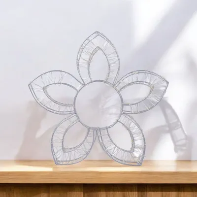 A decorative flower lamp is placed on a wooden shelf against a white wall.