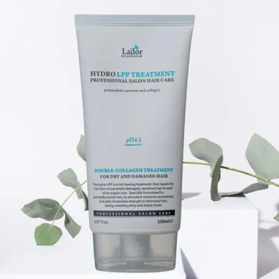 A tube of Lador Hydro LPP Treatment hair care product is displayed on a white pedestal, with green eucalyptus leaves in the foreground and background.