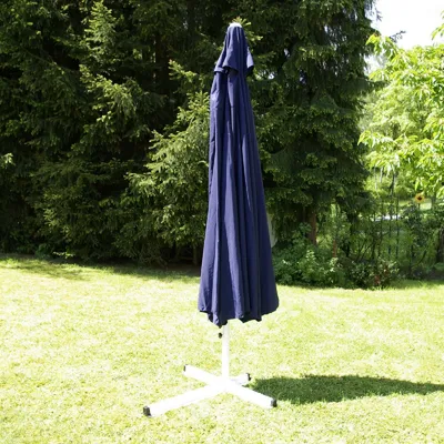 A closed blue umbrella with a white stand is set up on a green lawn with trees in the background.