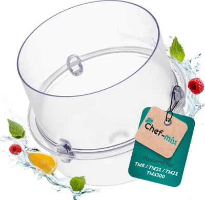 A clear plastic measuring cup with attached tags, surrounded by water splashes and fruit pieces.