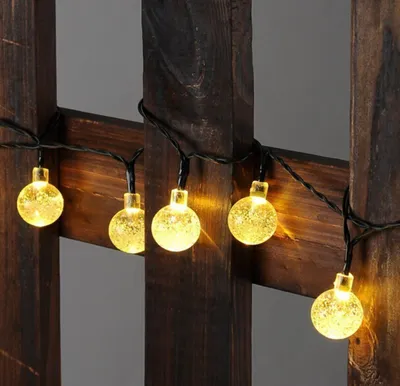A string of solar-powered LED lights with round, textured bulbs is draped over a dark wooden structure.