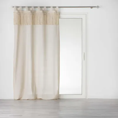 A cream-colored curtain with fringe detail hangs on a curtain rod in front of a sliding glass door.