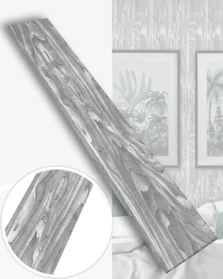 A single plank with a wood grain pattern is shown diagonally against a background of framed artwork and wallpaper.