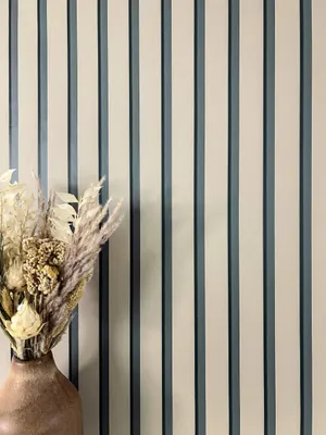 A vase with dried flowers is placed in front of a striped wall.