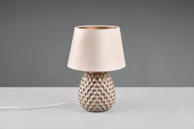 A table lamp with a textured base and a fabric shade sits on a white surface against a gray background.
