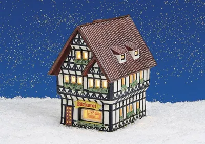 A miniature bakery building illuminated by internal lights, set against a snowy ground and a starry night sky.
