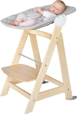 A baby is lying in a bouncer seat attached to a wooden high chair.