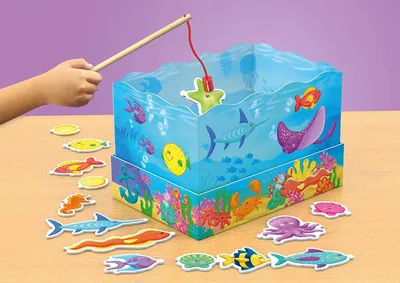 A child's hand is shown playing with a magnetic fishing game featuring sea creatures inside a clear box that simulates an aquarium.
