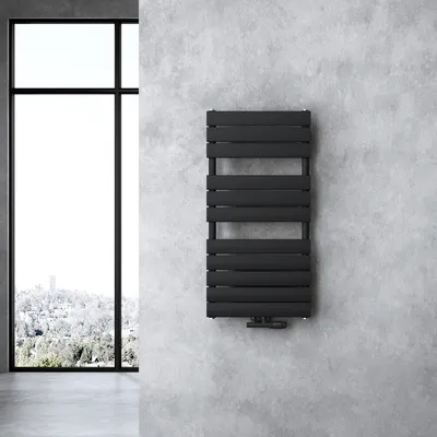 A black radiator is mounted on a textured gray concrete wall next to a large window.