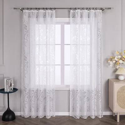 A white lace curtain with a rose pattern hangs in front of a window.