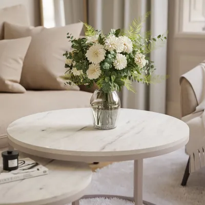 A floral arrangement in a glass vase sits on a marble coffee table in a living room.