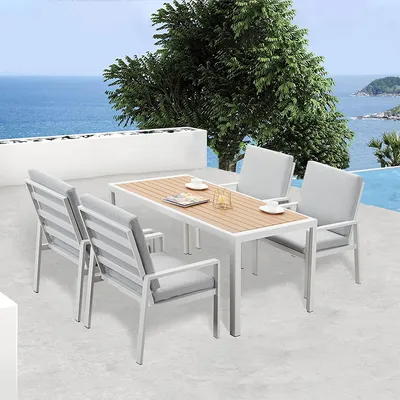 An outdoor dining set with a table and four chairs is placed on a patio overlooking the ocean.