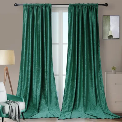 Two dark teal velvet curtains are shown hanging from a curtain rod in front of a window. A floor lamp and a chair are visible to the left, and a dresser with a small plant and artwork is visible to the right.