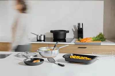 A person is blurred in the background of a kitchen scene, with various cookware and ingredients on the counter.