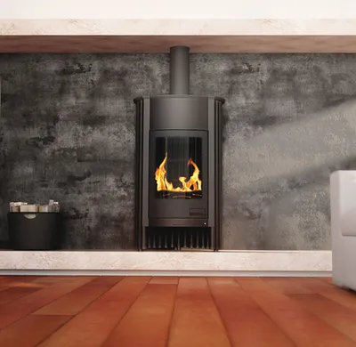 A modern living room with a black wood-burning stove as the focal point, set against a textured gray wall and a light-colored shelf. The floor is made of warm-toned wooden planks.