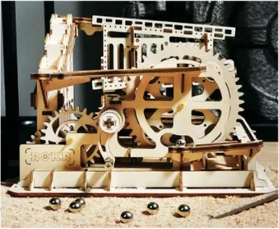 A wooden marble run model with several marbles scattered around it.