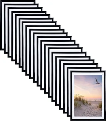 A stack of black picture frames arranged diagonally, with one frame showing a beach scene at sunset.