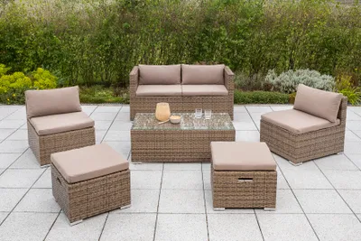 A set of outdoor furniture, including a sofa, two chairs, and two ottomans, arranged on a paved patio with greenery in the background.