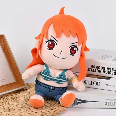 A plush toy of the character Nami from One Piece is sitting on a woven mat, with books in the background.