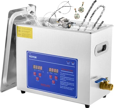 A stainless steel ultrasonic cleaner with a digital display and various items inside, including jewelry, glasses, and a wrench.