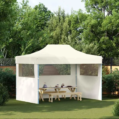 A cream-colored party tent set up on a green lawn, with wooden picnic tables and benches inside.