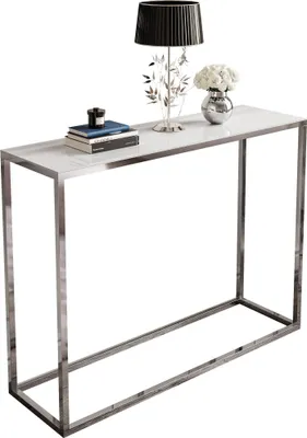 A console table with a white glass top and a chrome frame, decorated with a lamp, books, and a vase of flowers.