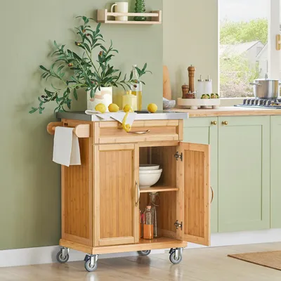 A kitchen scene with a wooden kitchen cart, green cabinets, and a window.