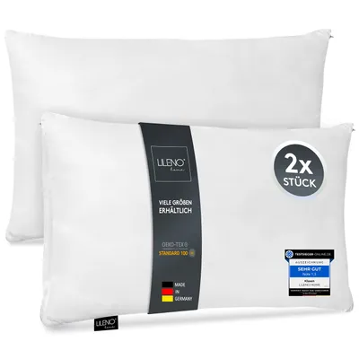 Two white pillows are shown, one slightly behind the other. A dark band with branding and product information is wrapped around the front pillow.