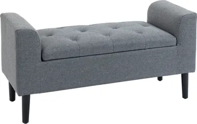 A gray upholstered storage bench with tufted seating and black wooden legs, shown against a white background.
