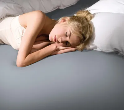 A woman sleeping in a bed with light gray sheets.