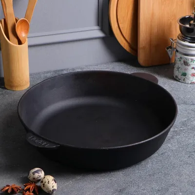 A black cast iron pan is placed on a gray countertop, with kitchen utensils and cutting boards in the background.