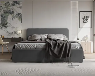 A modern bedroom with a large upholstered bed as the focal point, decorated with pillows and a throw blanket. A vanity table with a chair and a framed artwork on the wall complete the scene.