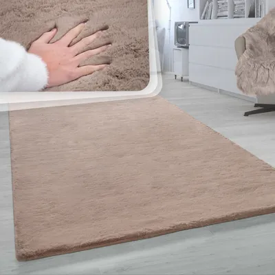 A hand is shown pressing into a soft, beige rug in a living room setting.