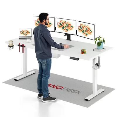 A man stands at a white standing desk with multiple monitors and a laptop.